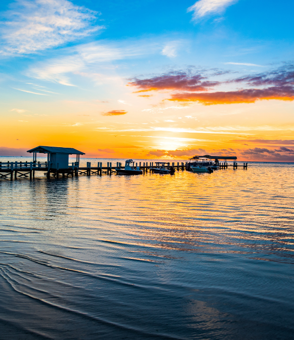 Islamorada vacation rentals at sunset with turquoise water, palm trees, a waterfront home, dock, and fishing boat