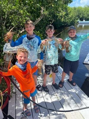Four young Florida Keys mini-season divers showing their lobster catch on a dock